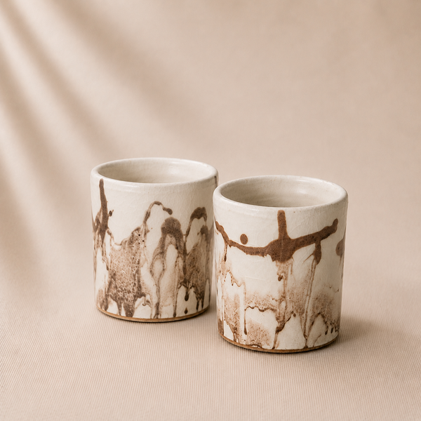 Two ceramic cups with abstract brown designs on a beige background