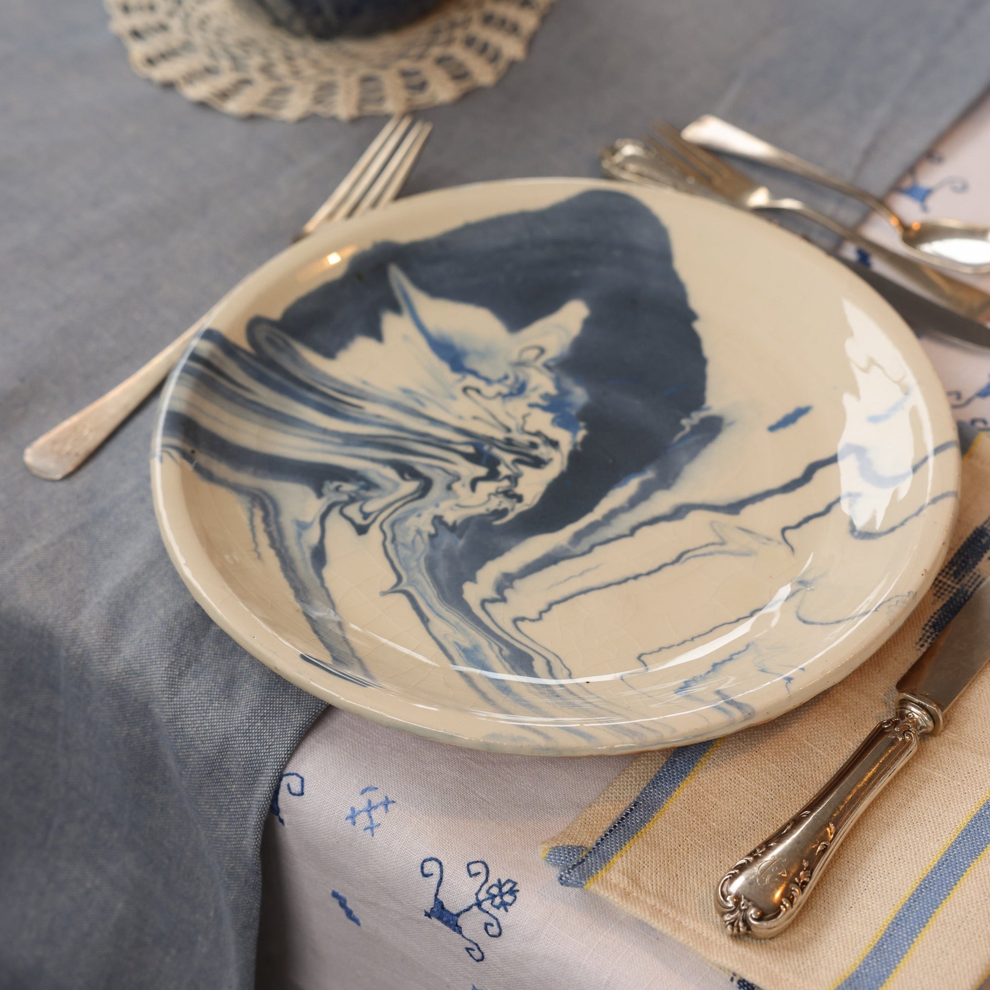 Table setting with a ceramic plate featuring blue abstract design on a gray tablecloth. - lifestyle