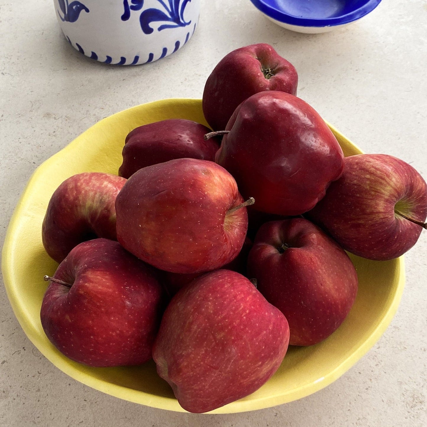 Yellow bowl filled with red apples on a light surface - lifestyle