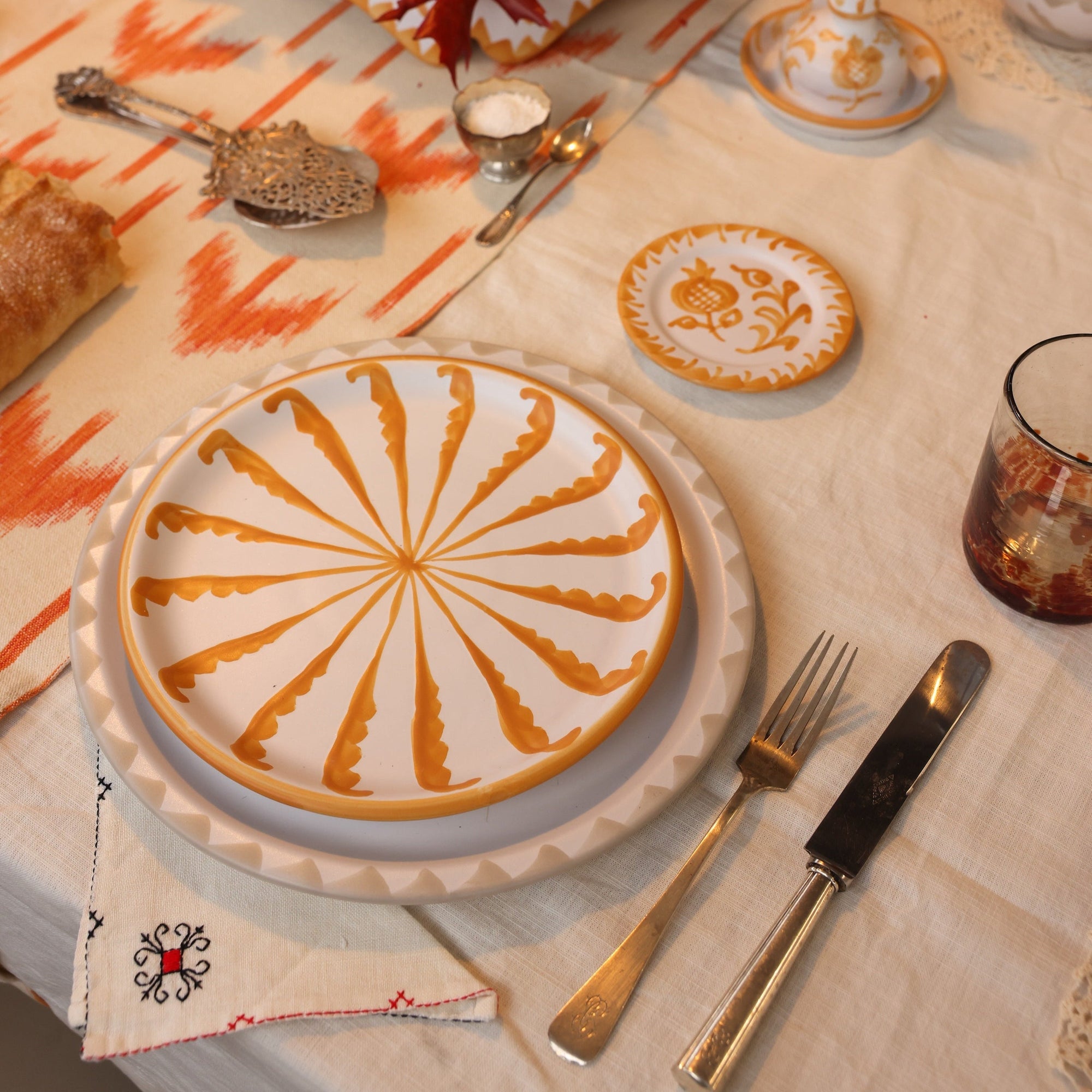 Dining table setting with decorative plates, cutlery, and a glass on a patterned tablecloth. - lifestyle