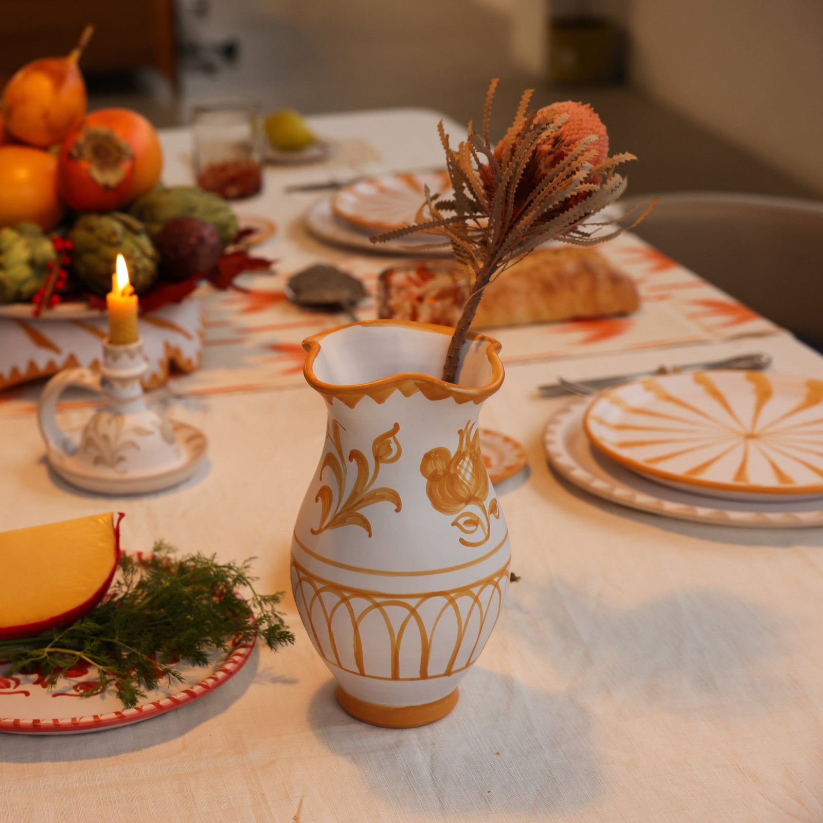 Decorative table setting with a vase, fruit, and candles on a tablecloth. - lifestyle