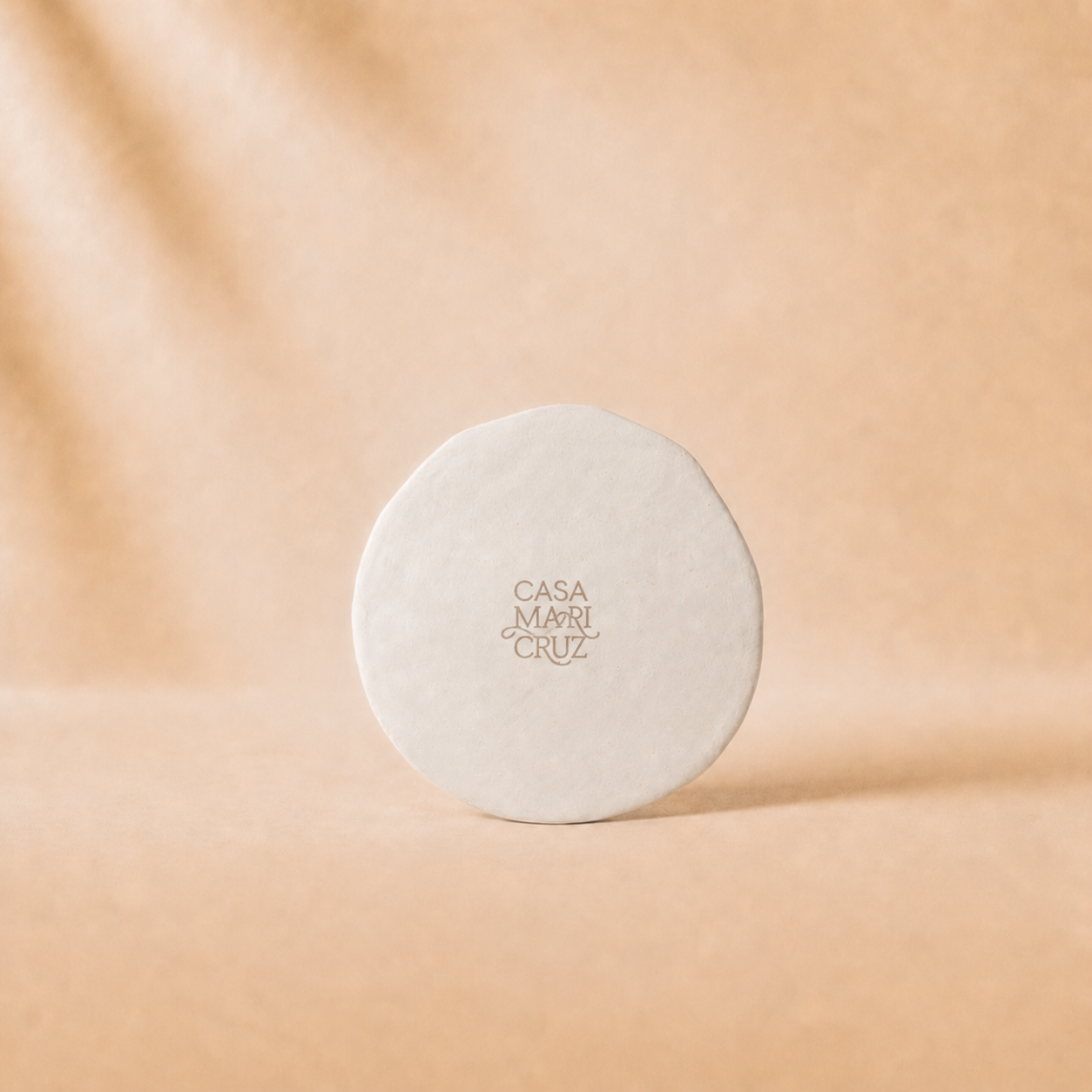Round beige product with 'Casa Mari Cruz' branding on a beige background - lifestyle
