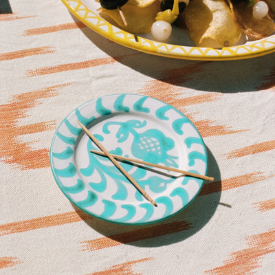Teal and white decorative plate with toothpicks on a patterned tablecloth - lifestyle