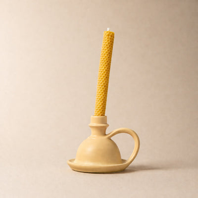 Beige candle holder with a yellow candle on a beige background
