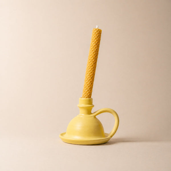 Yellow candle holder with a textured yellow candle on a beige background