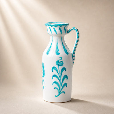 White ceramic pitcher with turquoise floral patterns on a beige background