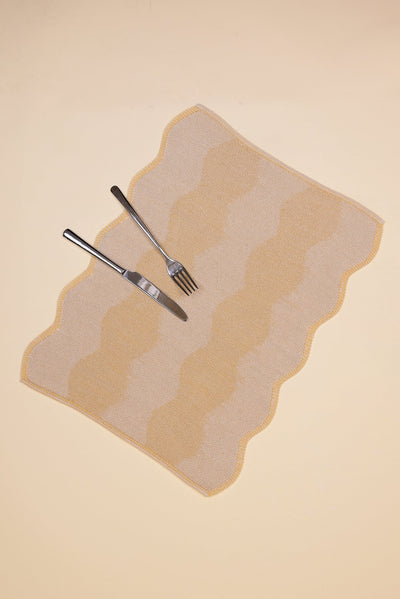 top view of beige and yellow knit organic cotton and hemp table mat with wavy pattern with cutlery 