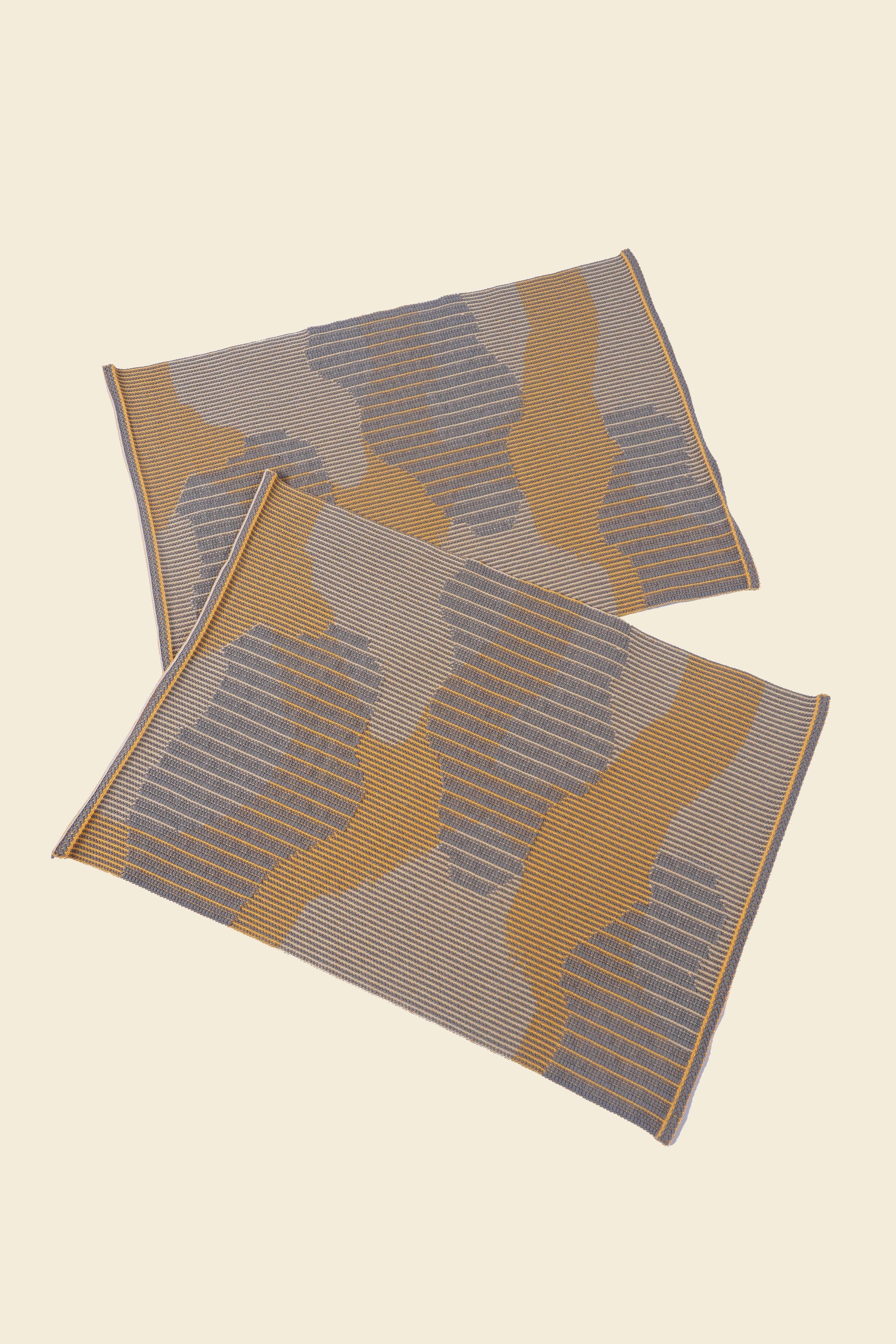 top view of yellow knit organic cotton table mat with abstract design in pair