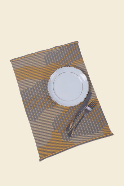 top view of yellow knit organic cotton table mat with abstract design with plate