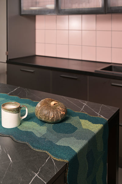 side view of green knit organic cotton and viscose table runner with abstract pattern and wavy edges kitchen display