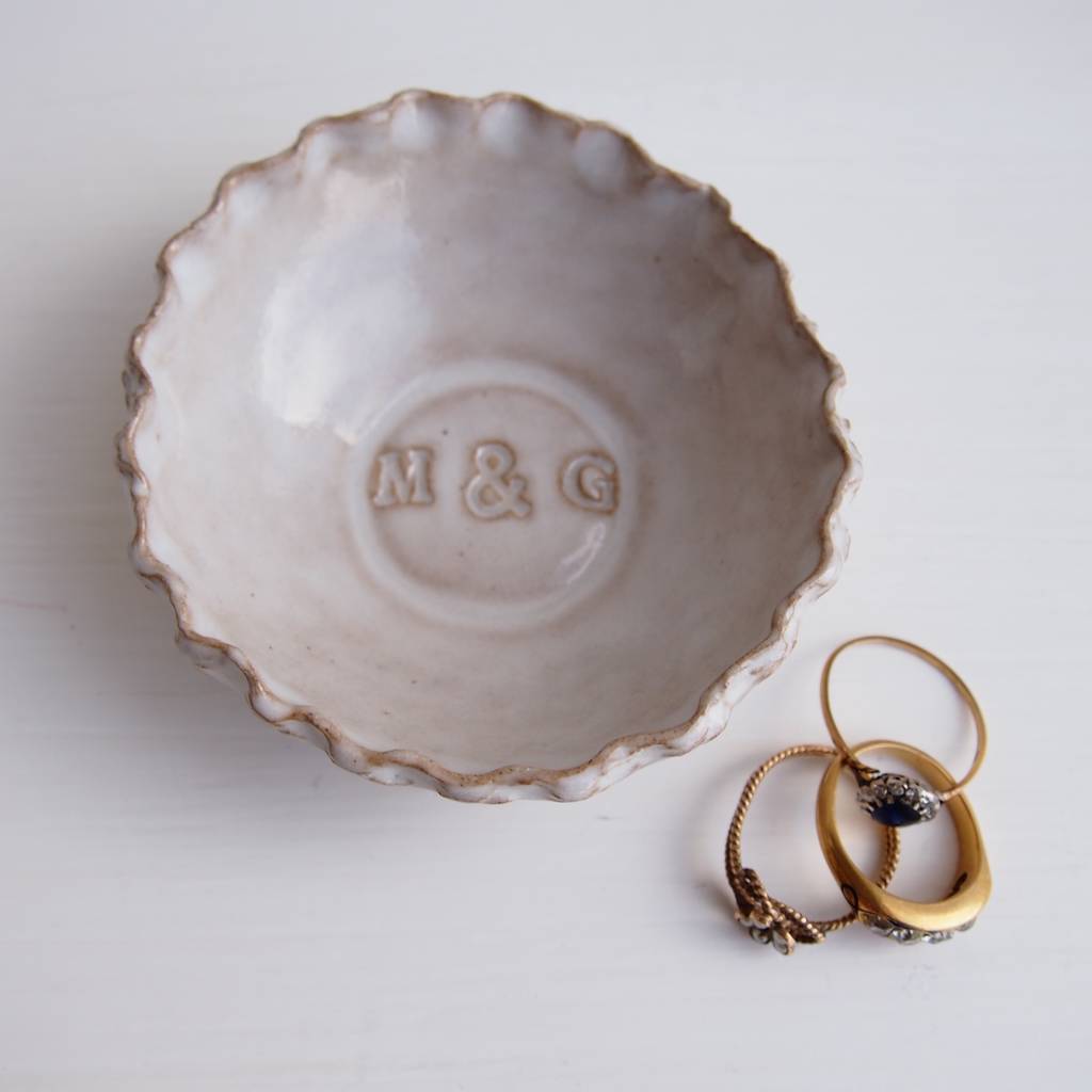 Ceramic jewelry dish with 'M & G' initials and two gold rings on a white background