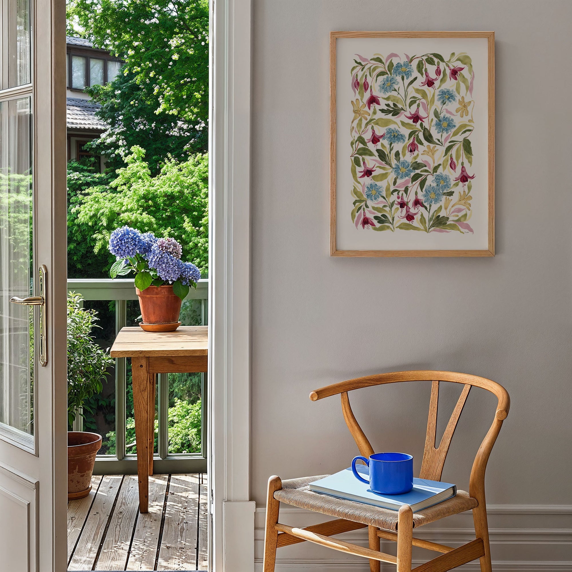 fuchsia print styled on blank wall by a chair, door open to show garden view with wooden table and plant pots on.