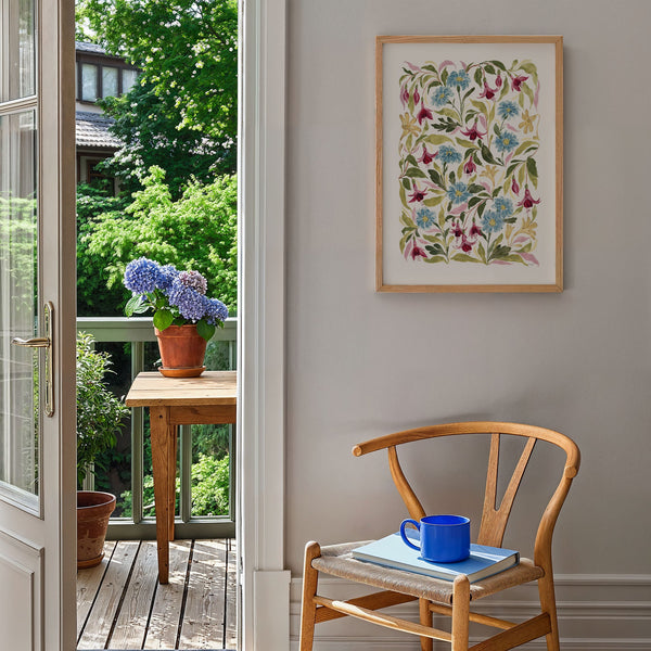 fuchsia print styled on blank wall by a chair, door open to show garden view with wooden table and plant pots on.
