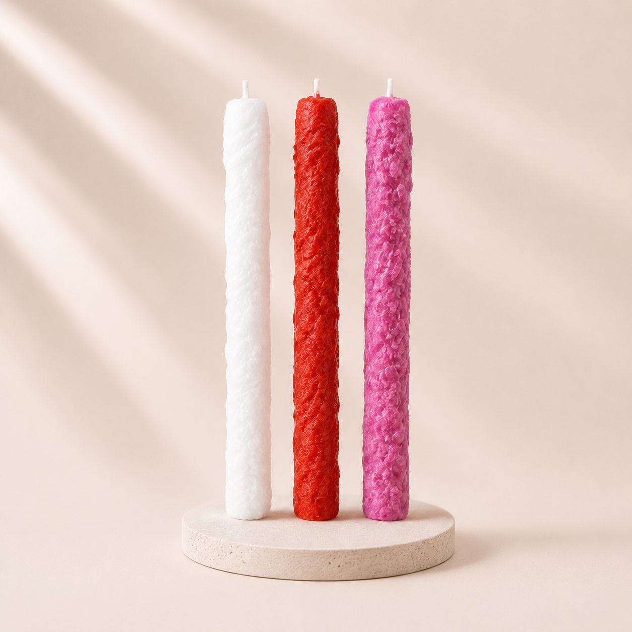 Three textured candles in white, red, and pink on a beige stand against a beige background