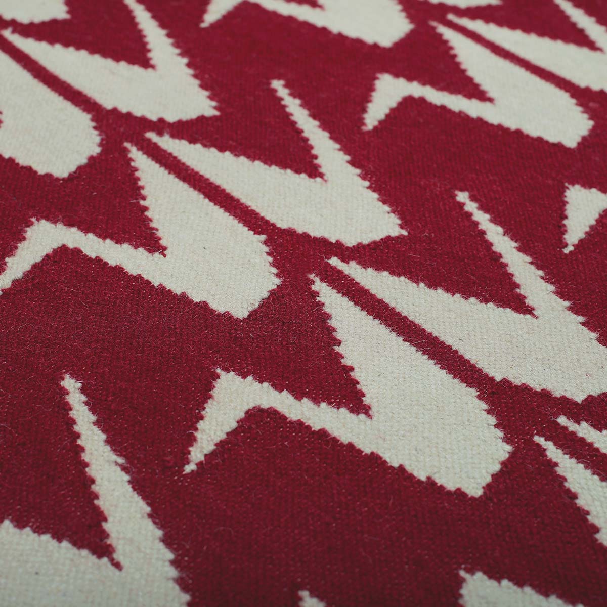 Detail of handwoven Maroon rug handwoven in wool with grey crane motifs on a rich red base.