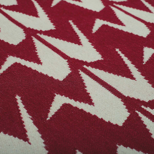 Detail of handwoven Maroon rug handwoven in wool with grey crane motifs on a rich red base.