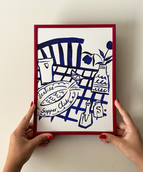 Seaside Supper Club ink painting, fish dinner on checked tablecloth in frame being held