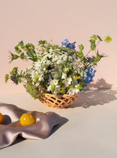 An orange ceramic basket with wildflowers sits next to a soft cloth on a pale surface.