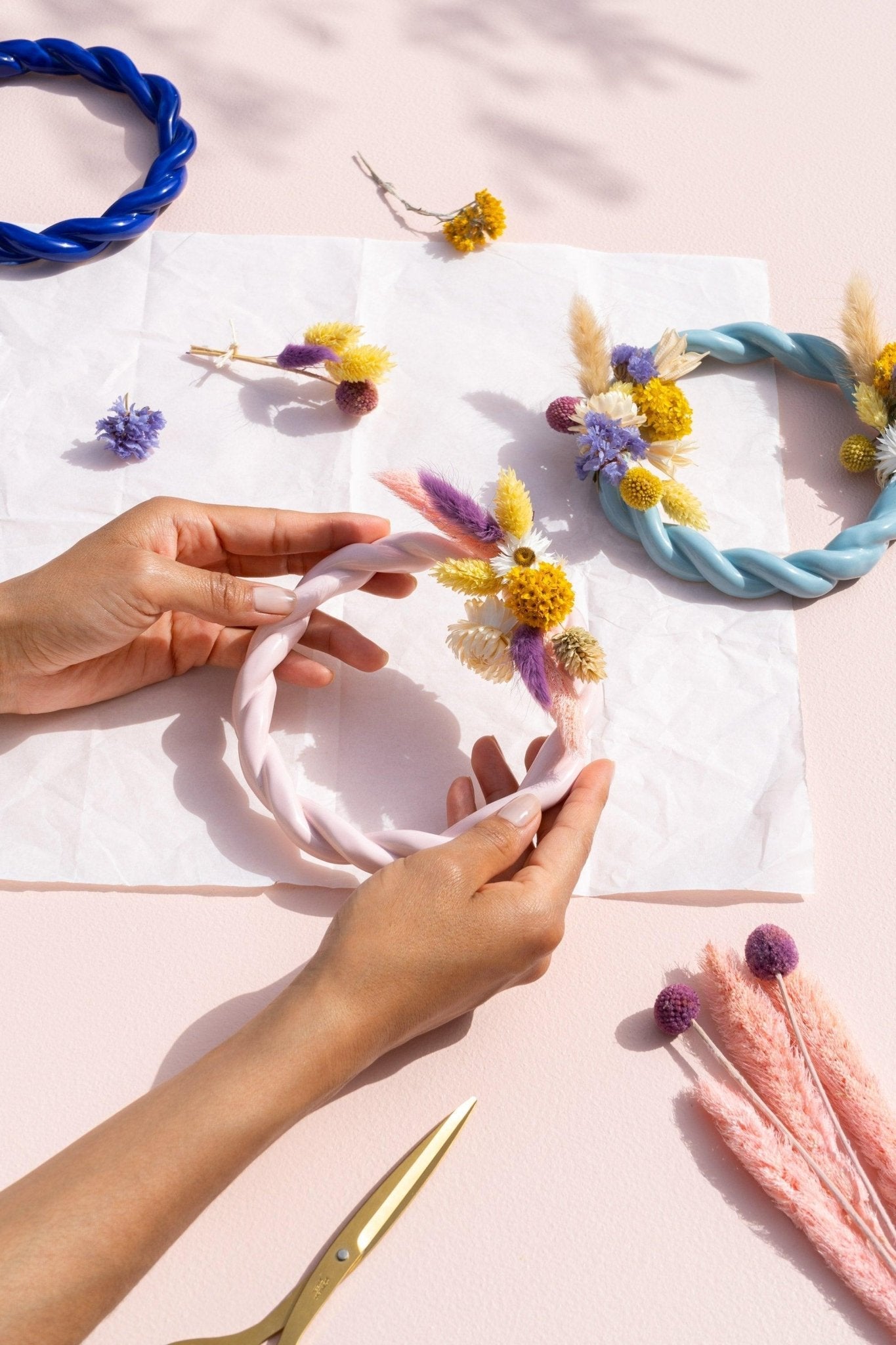 Hands decorating a pink and light blue twisted OCTAEVO Sicilia trivet with dried flowers. 