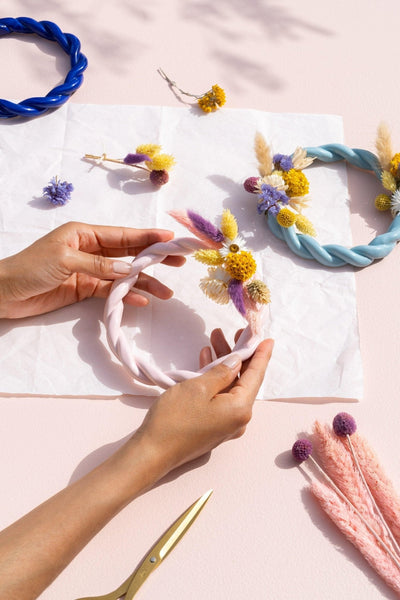 Hands decorating a pink and light blue twisted OCTAEVO Sicilia trivet with dried flowers. 