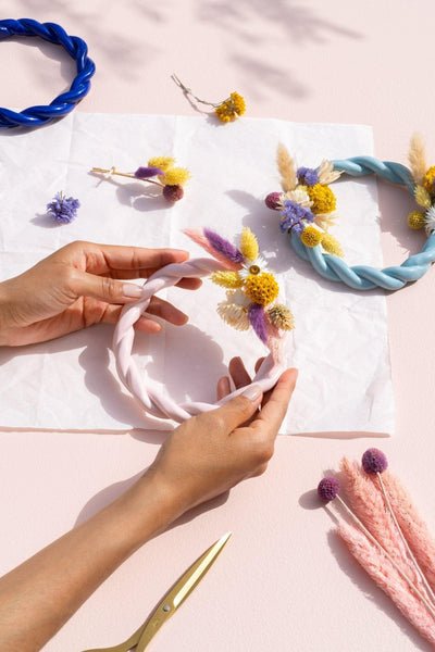 Hands decorating a pink and light blue twisted OCTAEVO Sicilia trivet with dried flowers. 