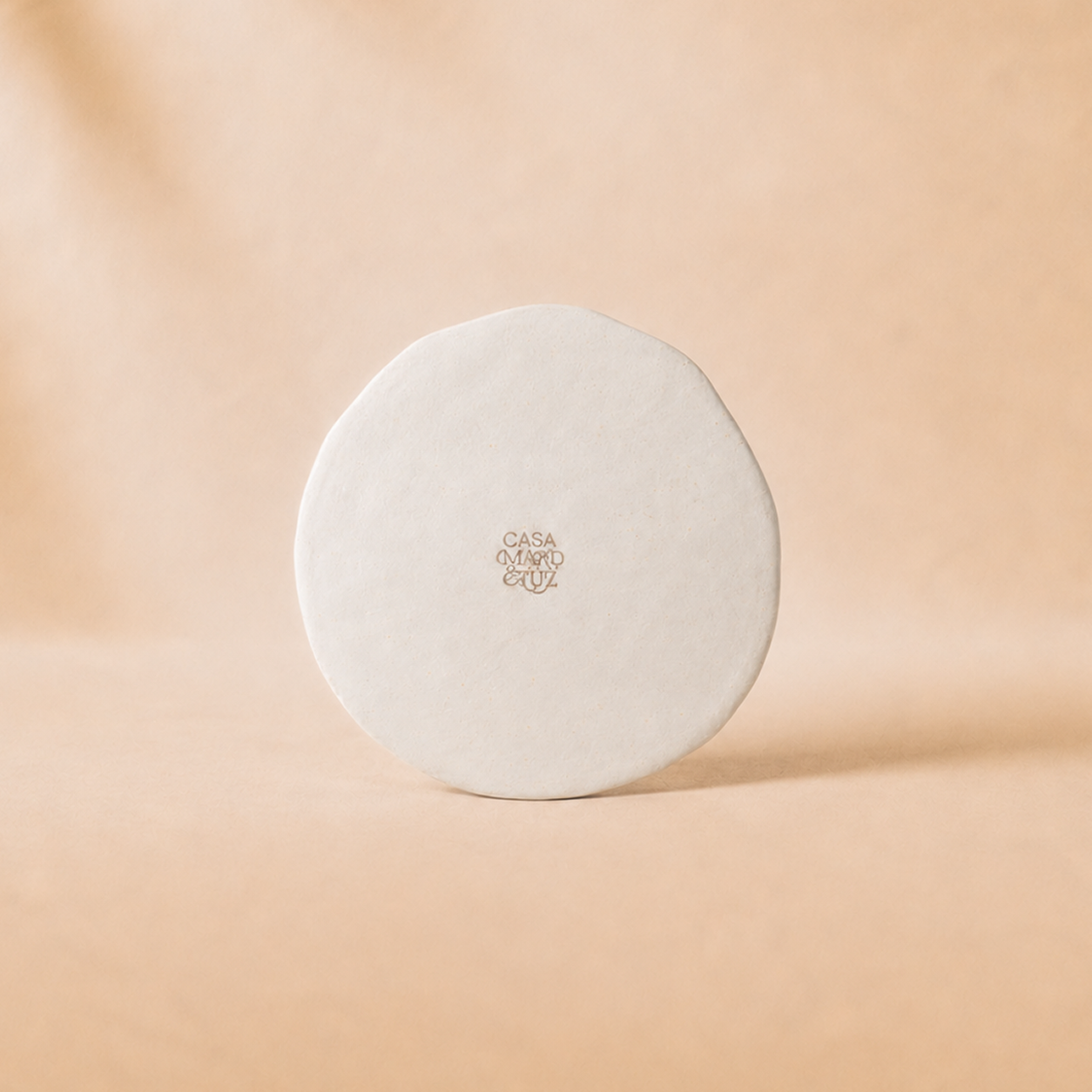 Round white object with 'Casa' branding on a beige background - lifestyle