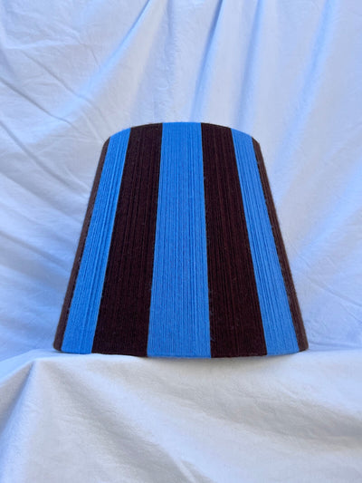A Slice Shades handmade yarn striped lampshade with alternating vertical stripes of blue and dark brown, displayed on a white fabric backdrop.