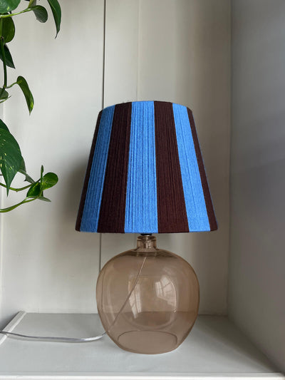 A Slice Shades handmade yarn striped lampshade with alternating vertical stripes of blue and dark brown, displayed on a white fabric backdrop.
