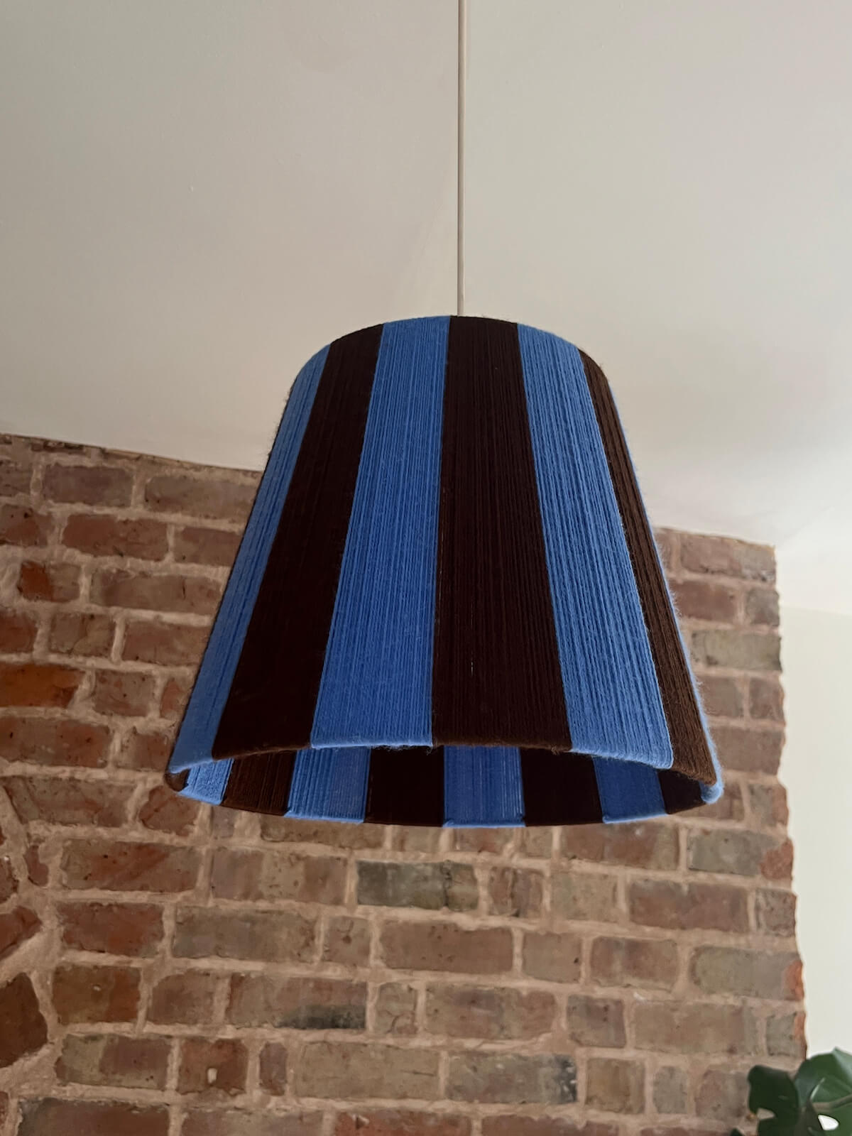 A Slice Shades handmade yarn striped lampshade with alternating vertical stripes of blue and dark brown, displayed on a white fabric backdrop.
