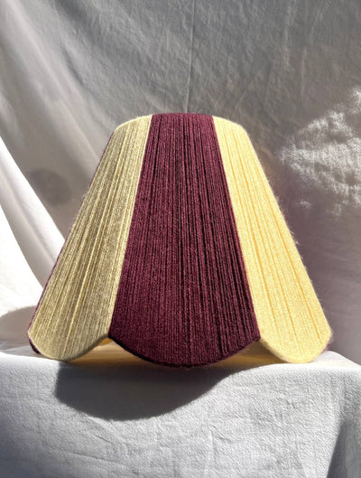 A Slice Shades lampshade with a handwoven yarn design of textured buttermilk yellow and deep burgundy, displayed on a draped white fabric background.