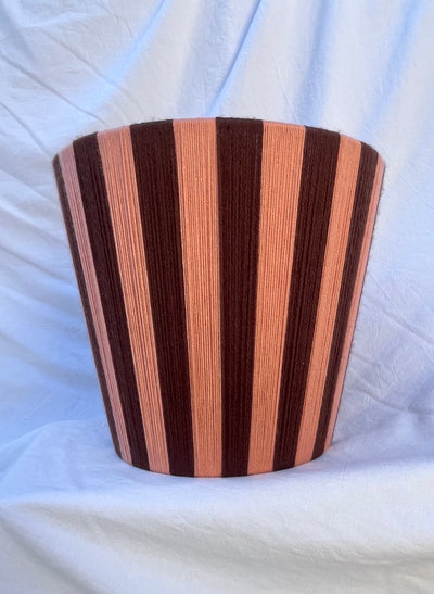 A Slice Shades handwoven striped yarn lampshade with alternating vertical stripes of dark brown and a warm peach-pink, displayed on a draped white fabric background.