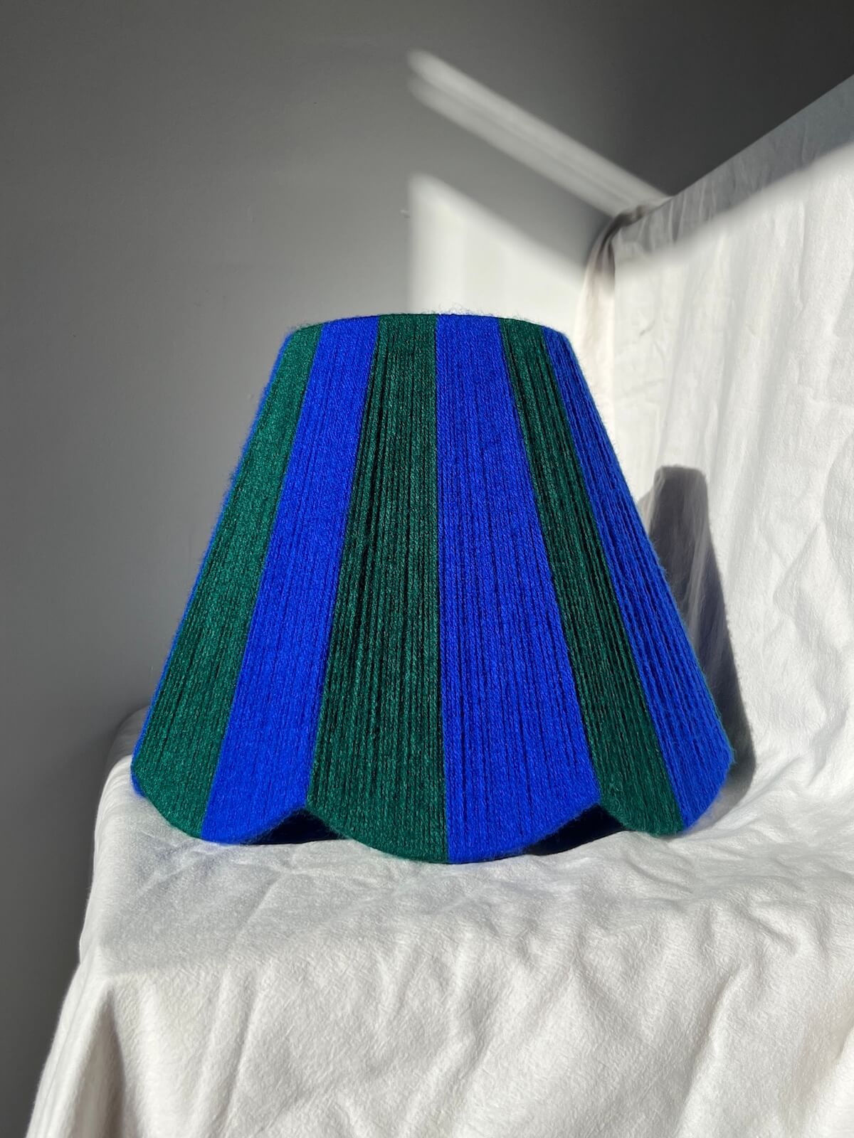 A Slice Shades handwoven yarn striped Scallop Lampshade in the sun in Cobalt Blue & Emerald Green.