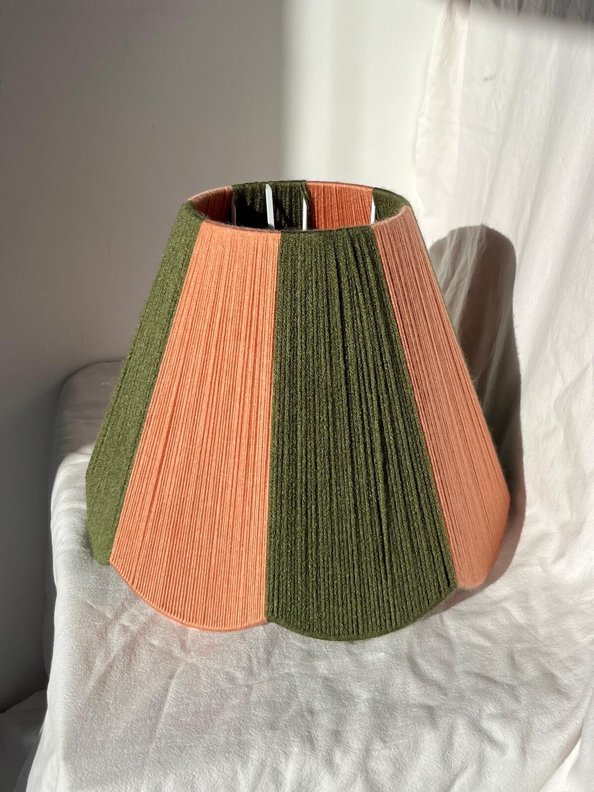 A slice shades handwoven striped scallop yarn lampshade in olive green and plaster pink with white background.