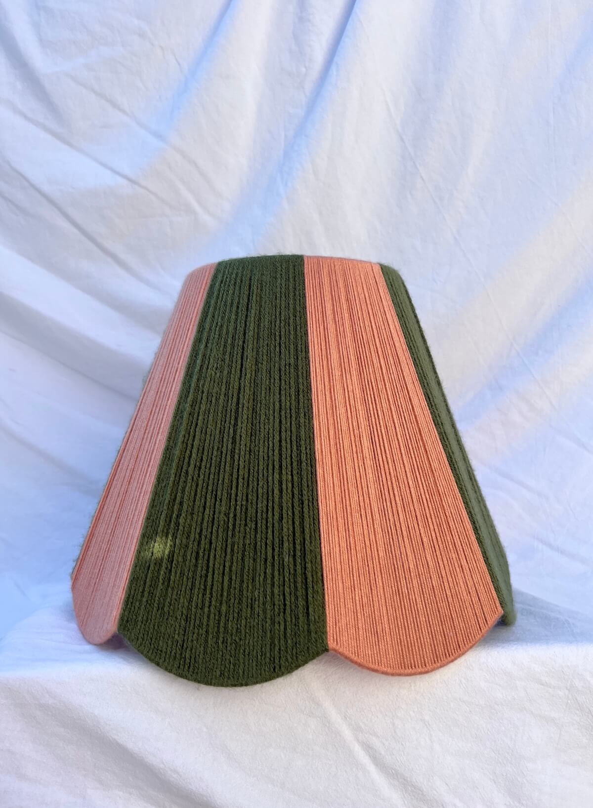 A slice shades handwoven striped scallop yarn lampshade in olive green and plaster pink with white background.