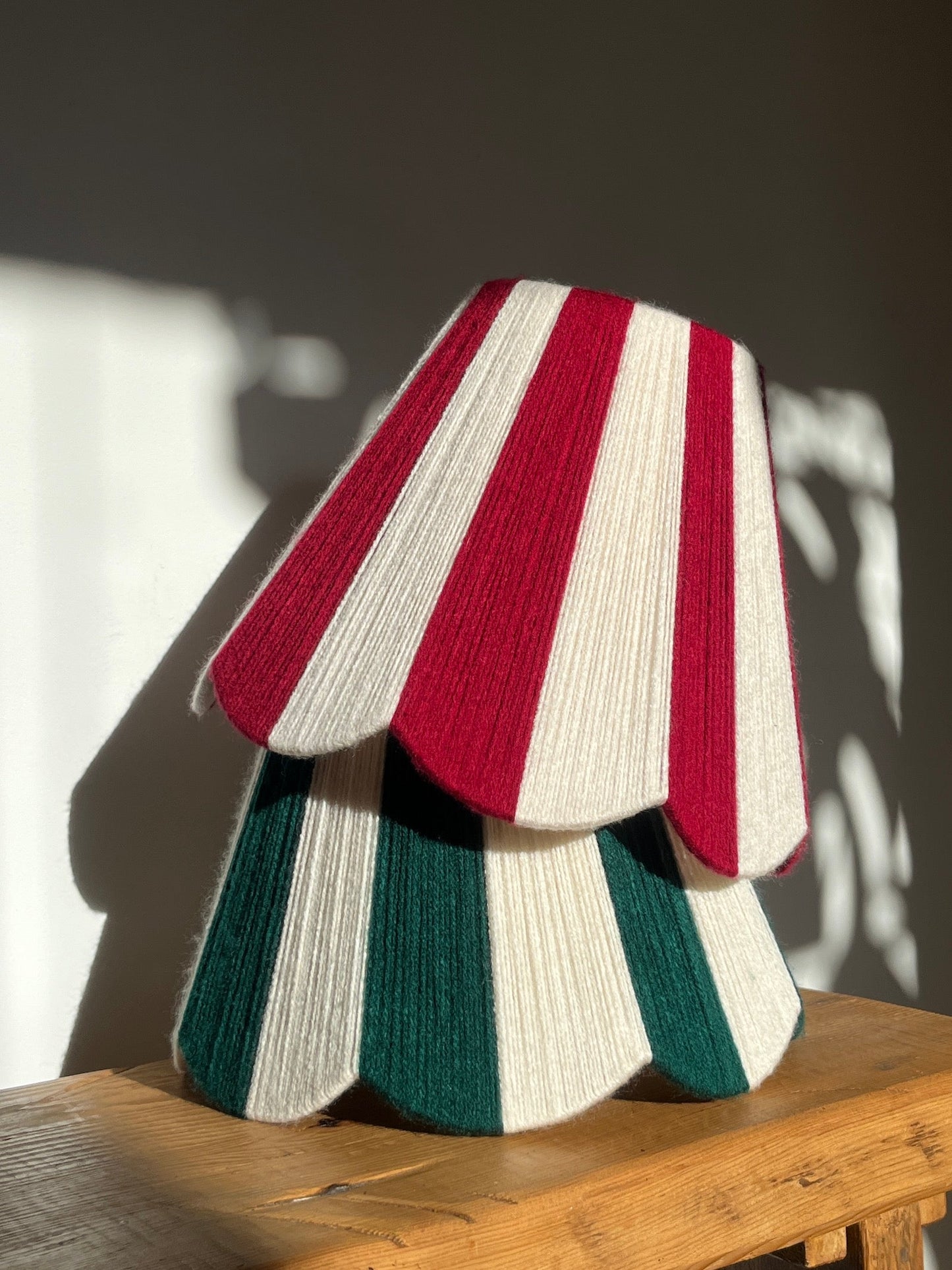 Slice Shades handwoven yarn string striped lampshades stacked in emerald green, ruby red  and ecru. Festive candy cane colourways sitting on a bench with shadows in sunlight.