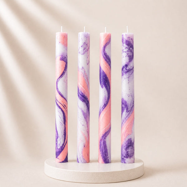 Four marbled candles in pink and purple on a white stand against a beige background