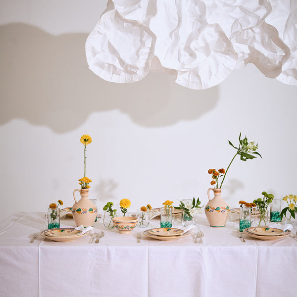 Decorative table setting with ceramic plates, glasses, and vases on a white tablecloth.