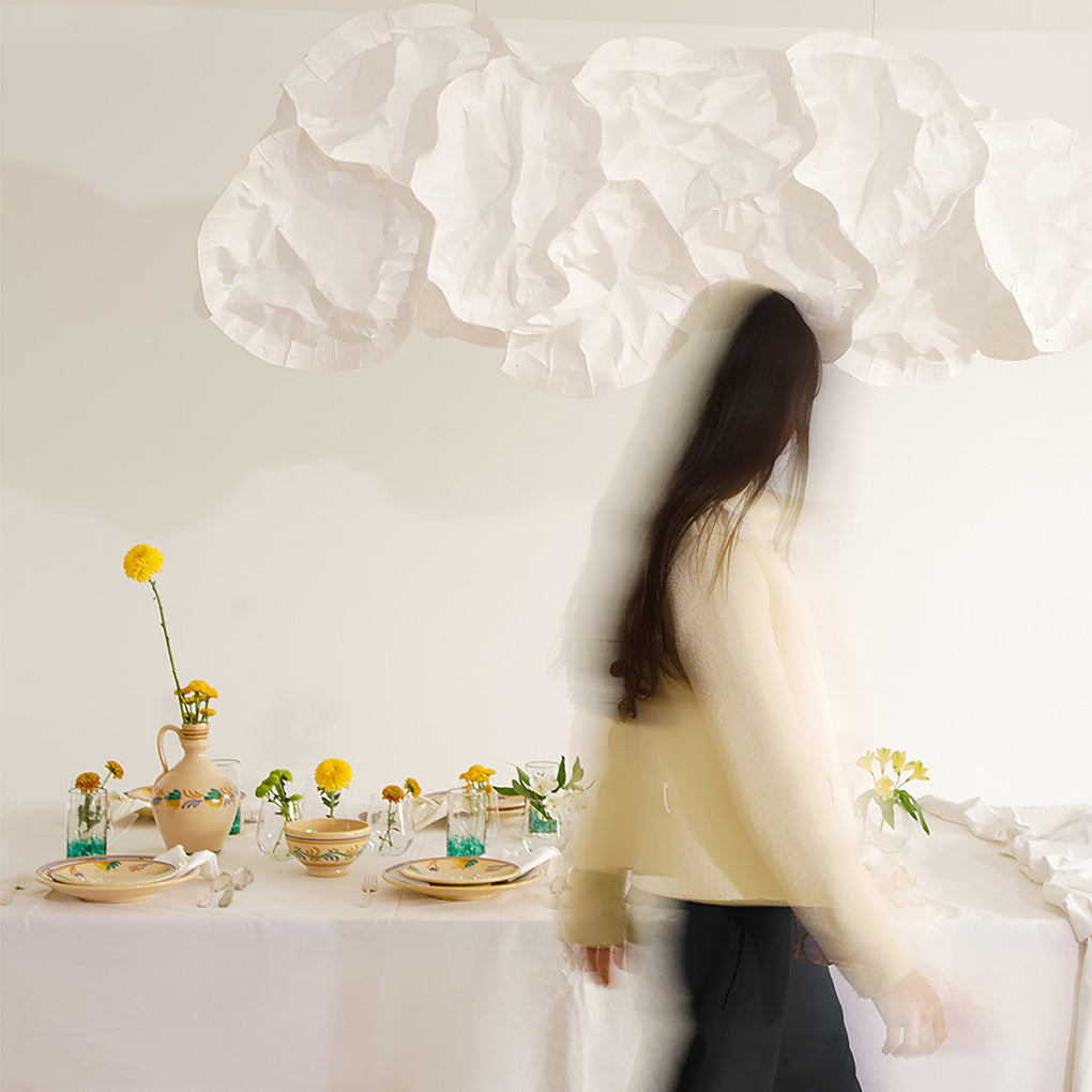 Woman standing in a room with a table set for a meal, featuring flowers and a vase -lifestyle