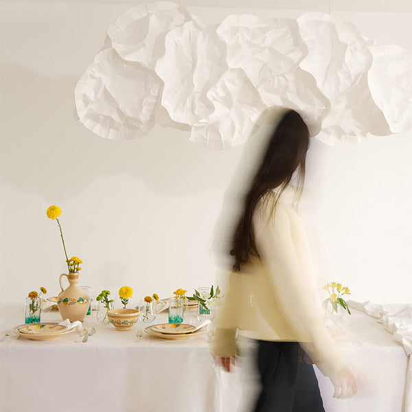 Woman standing in a room with a table set for a meal, featuring flowers and a vase -lifestyle
