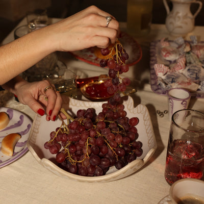 Person arranging grapes on a plate with a table setting in the background - lifestyle