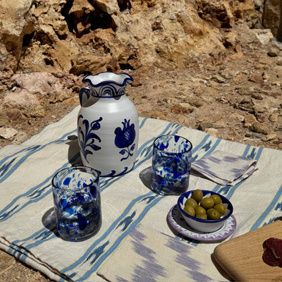 Ceramic pitcher and glasses on a tablecloth with a stone wall background - lifestyle