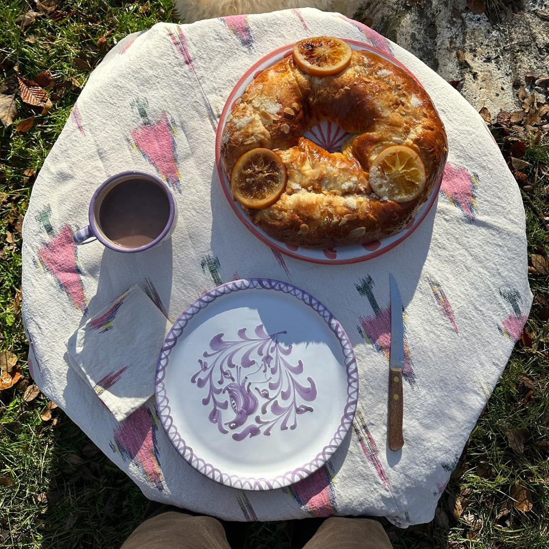 Round table with a cake, traditional dinner plate, linen, and a cup on a grassy surface with a dog nearby. - lifestyle
