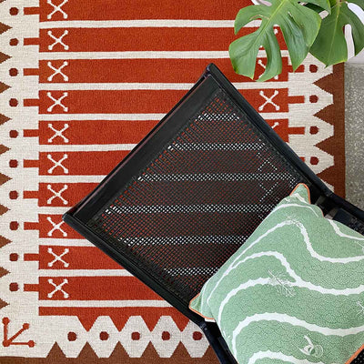 Rust Darjeeling Stripe rug handwoven in warm tones of orange, red and brown with chair and cushion.