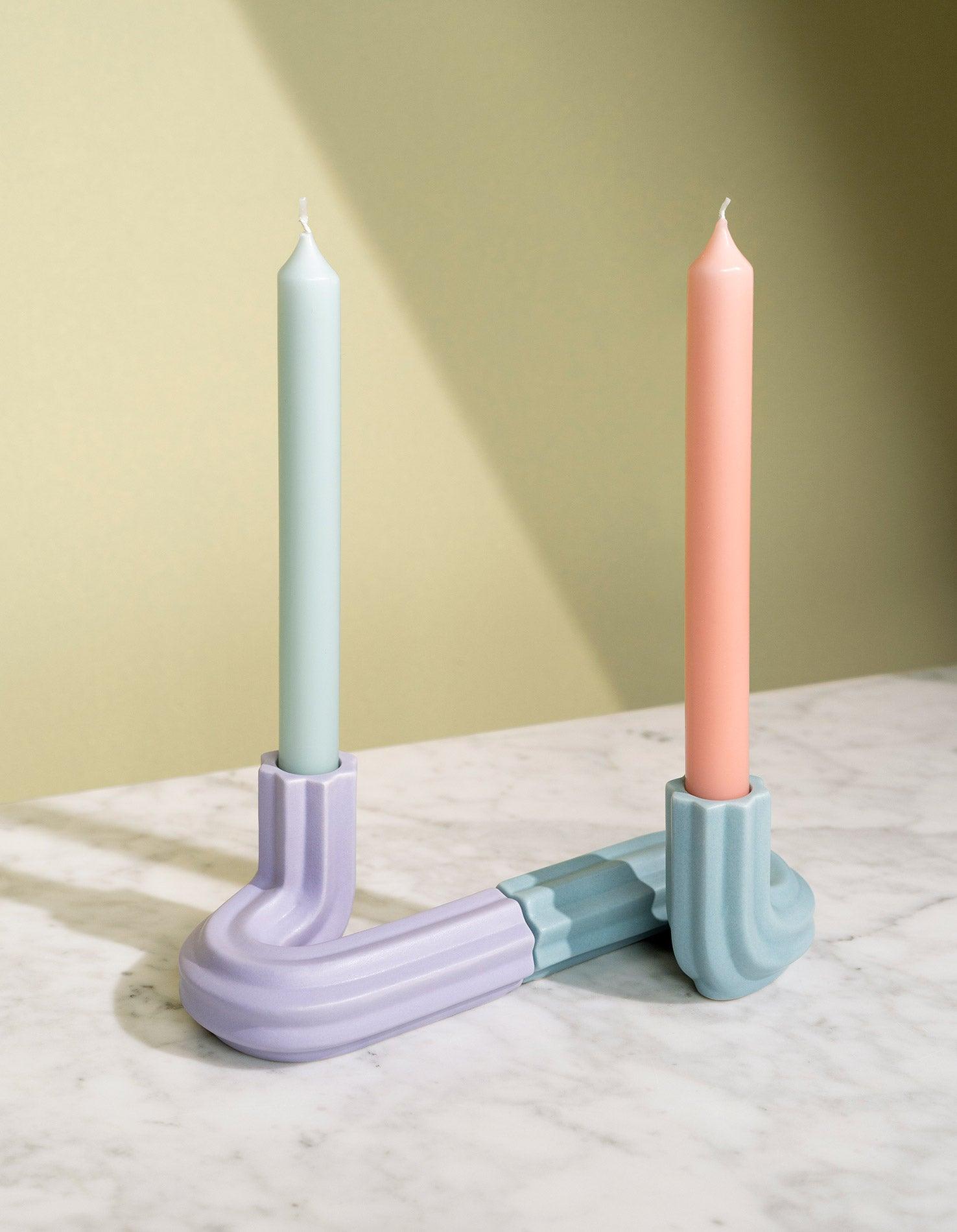 Two pastel candles in light blue OCTAEVO Templo Candle Holders on marble, set against a beige background.