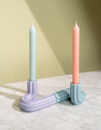 Two pastel candles in light blue OCTAEVO Templo Candle Holders on marble, set against a beige background.