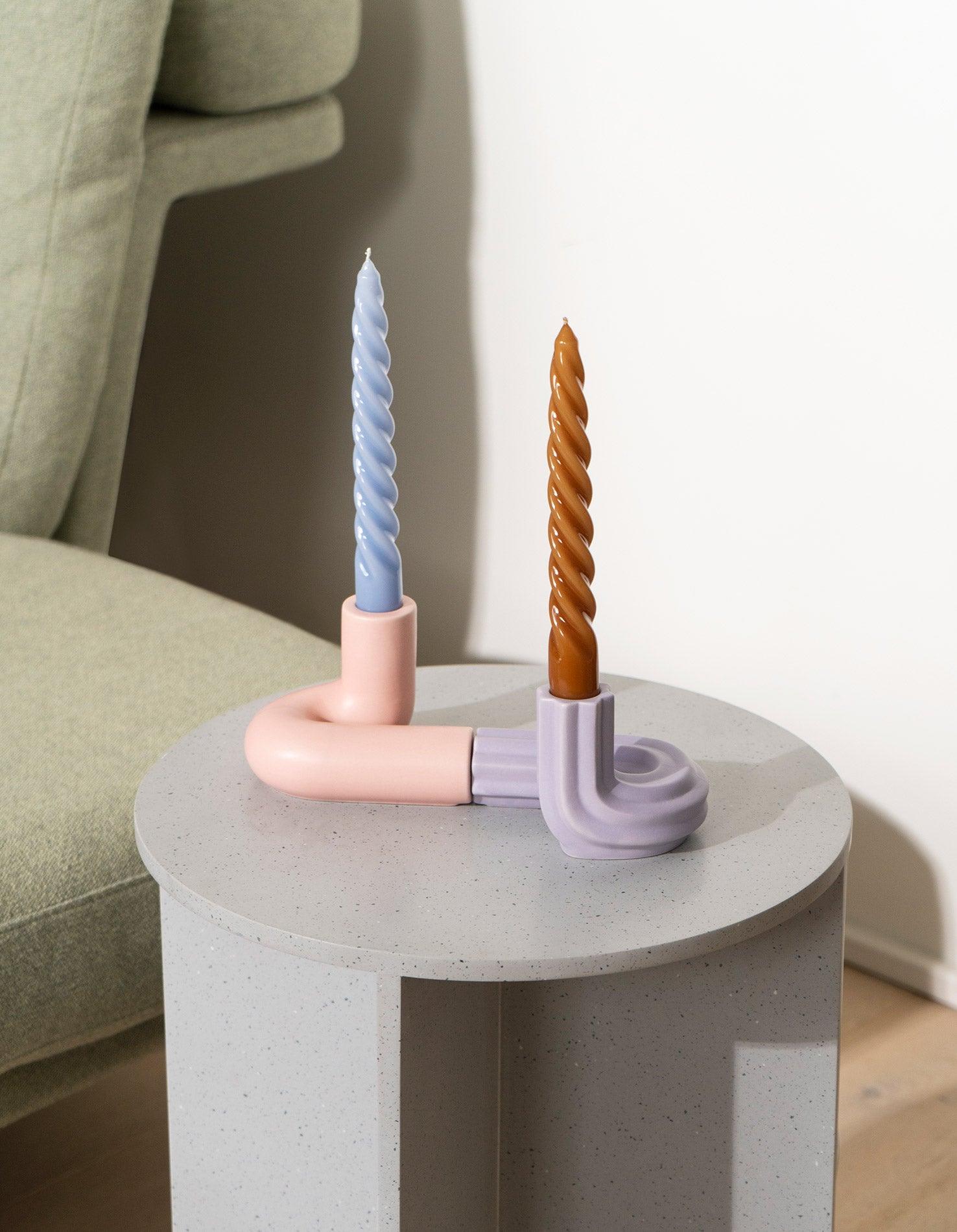 Two spiral candles in purple OCTAEVO Templo Candle Holders sit on a round table.