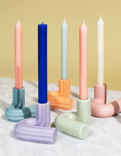 Five OCTAEVO Templo Candle Holders with colorful candles are arranged on a marble surface against a beige backdrop.