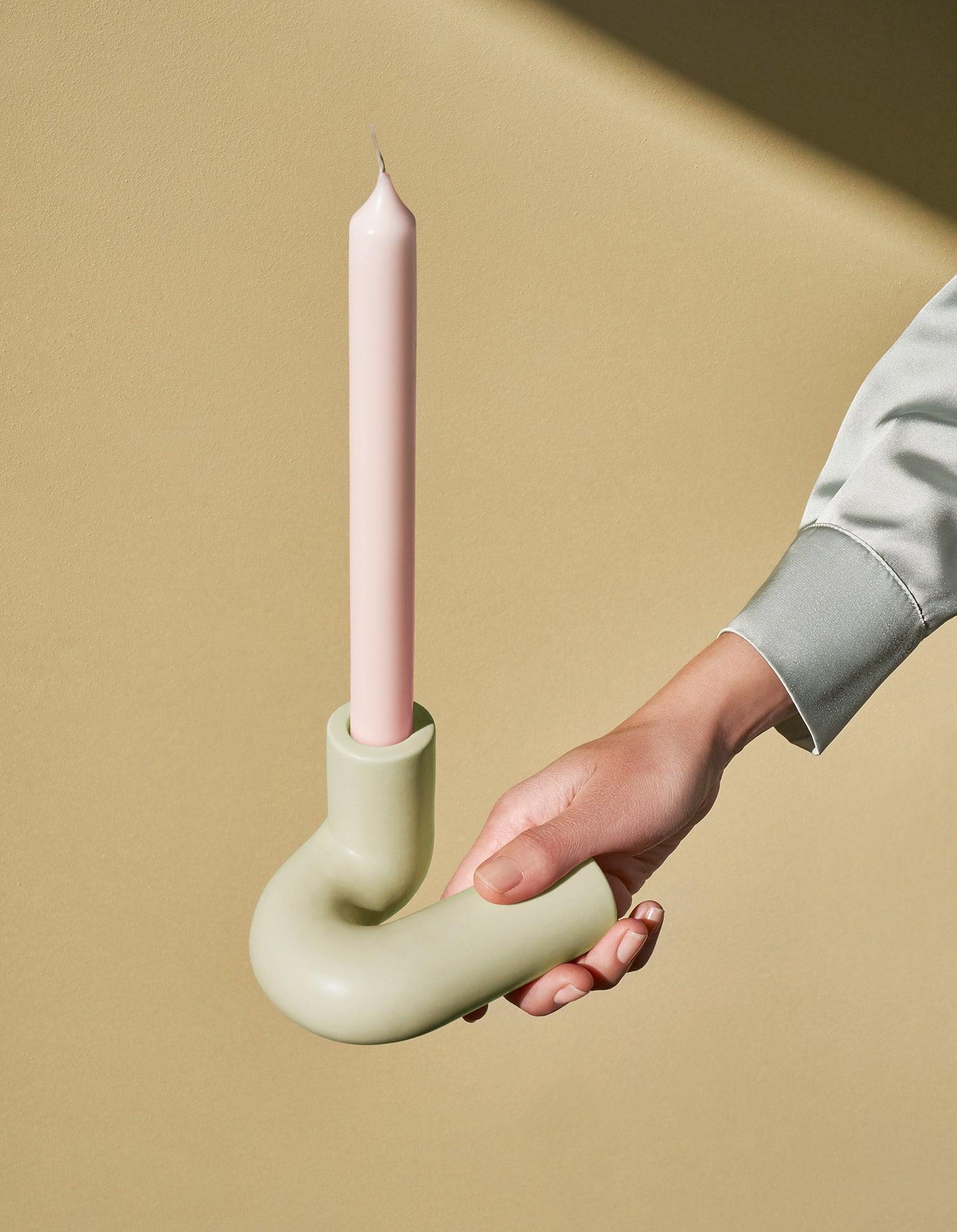 A hand holds the OCTAEVO light mint Templo Candle Holder with a pastel taper candle against a beige background.