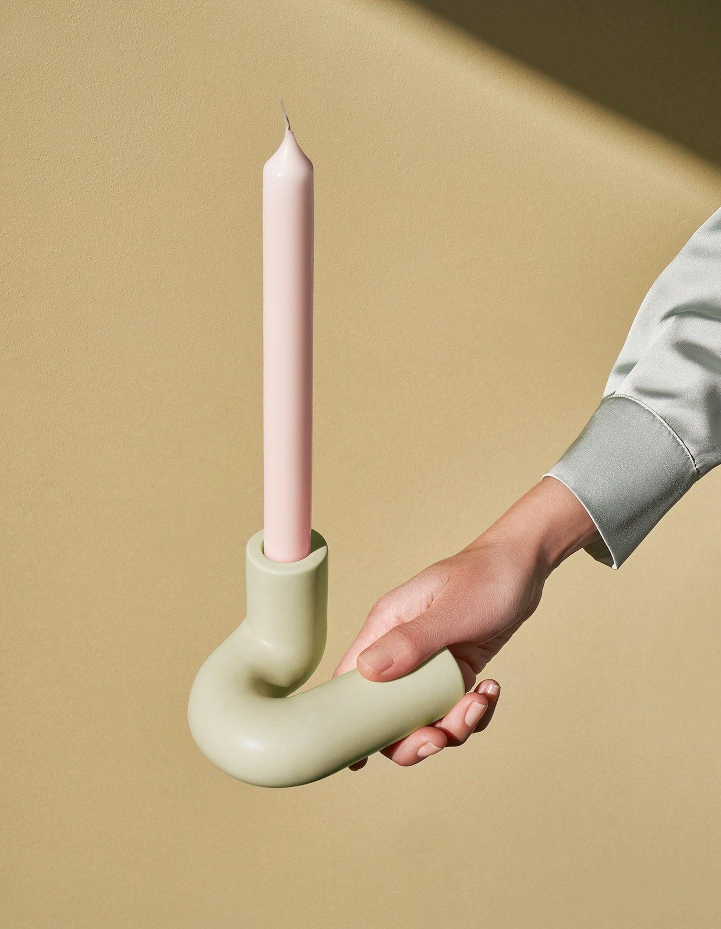 A hand holds the OCTAEVO light mint Templo Candle Holder with a pastel taper candle against a beige background.