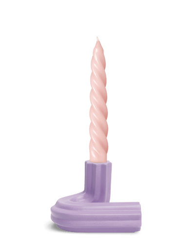 A pink twisted candle sits in OCTAEVO’s Templo Candle Holder, in Purple L-shaped ceramic piece, on a white background.